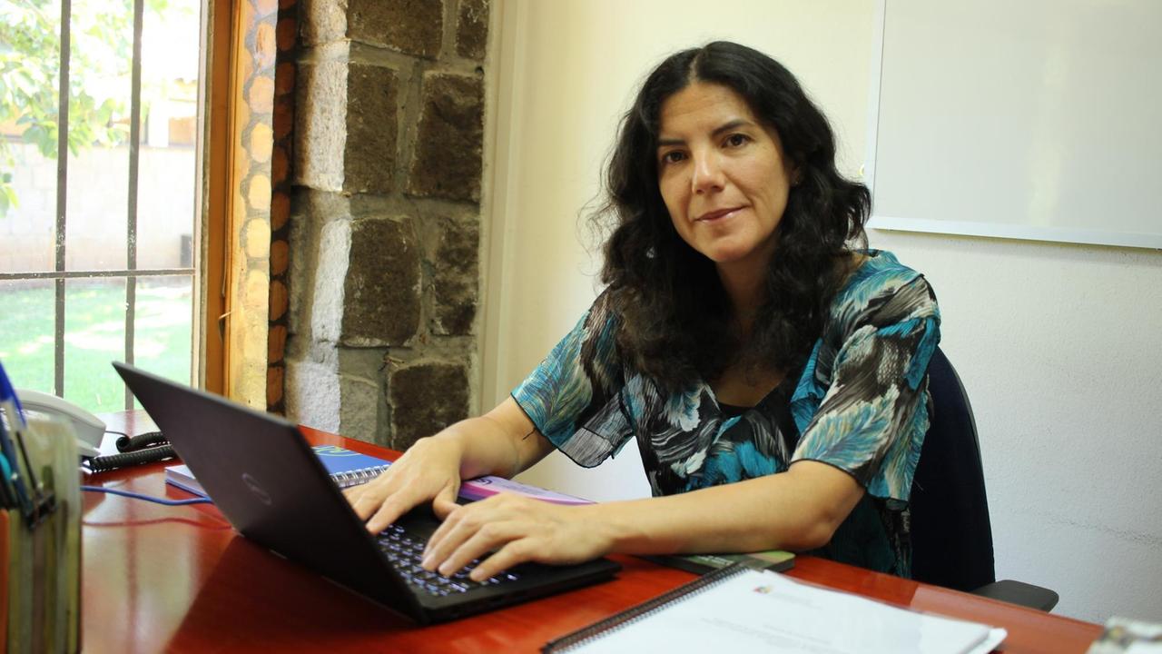 María Muñoz sitzt an ihrem Schreibtisch und schaut freundlich in die Kamera.