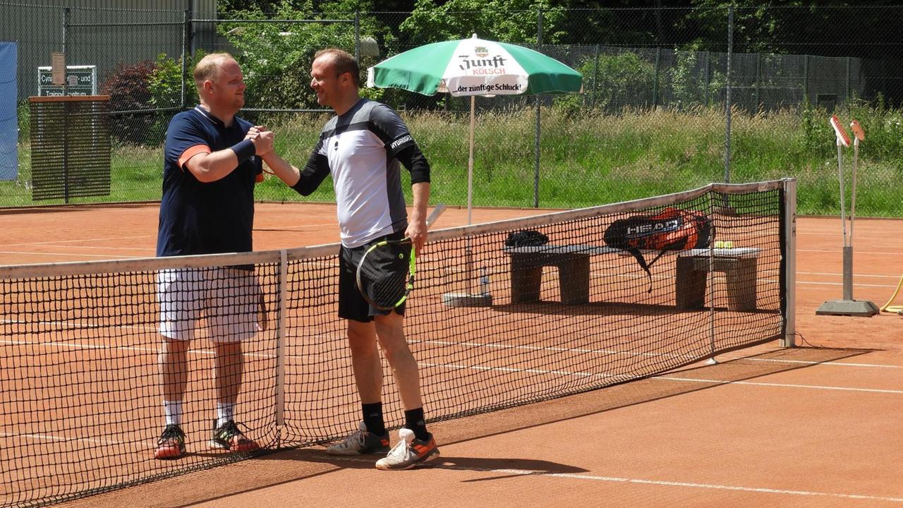 Zwei Tennisspieler geben sich am Netz auf dem Tennisplatz die Hand