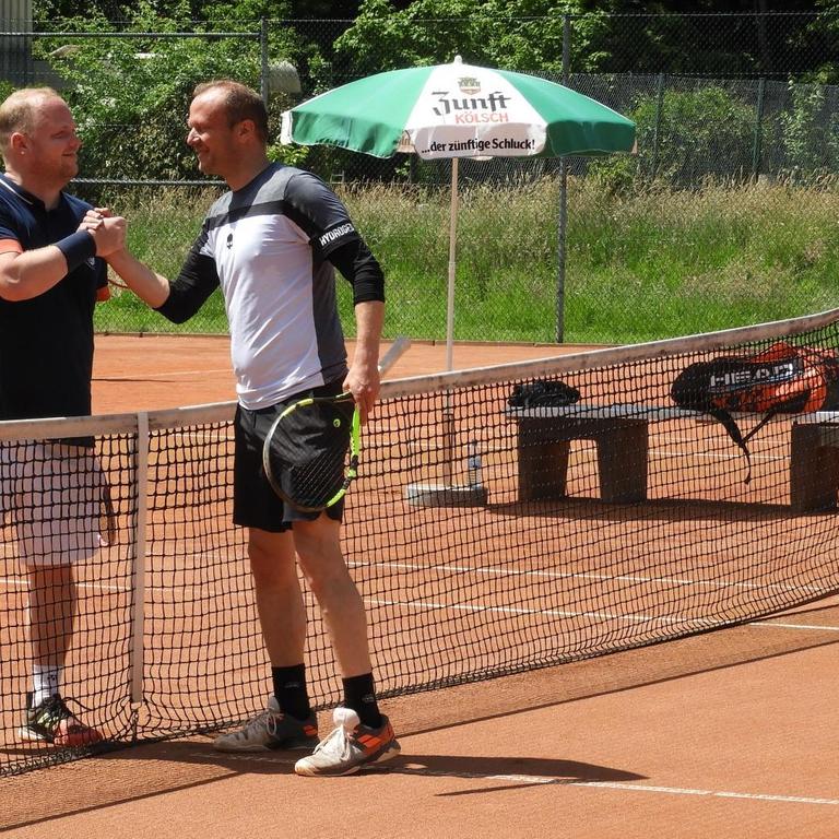 Zwei Tennisspieler geben sich am Netz auf dem Tennisplatz die Hand