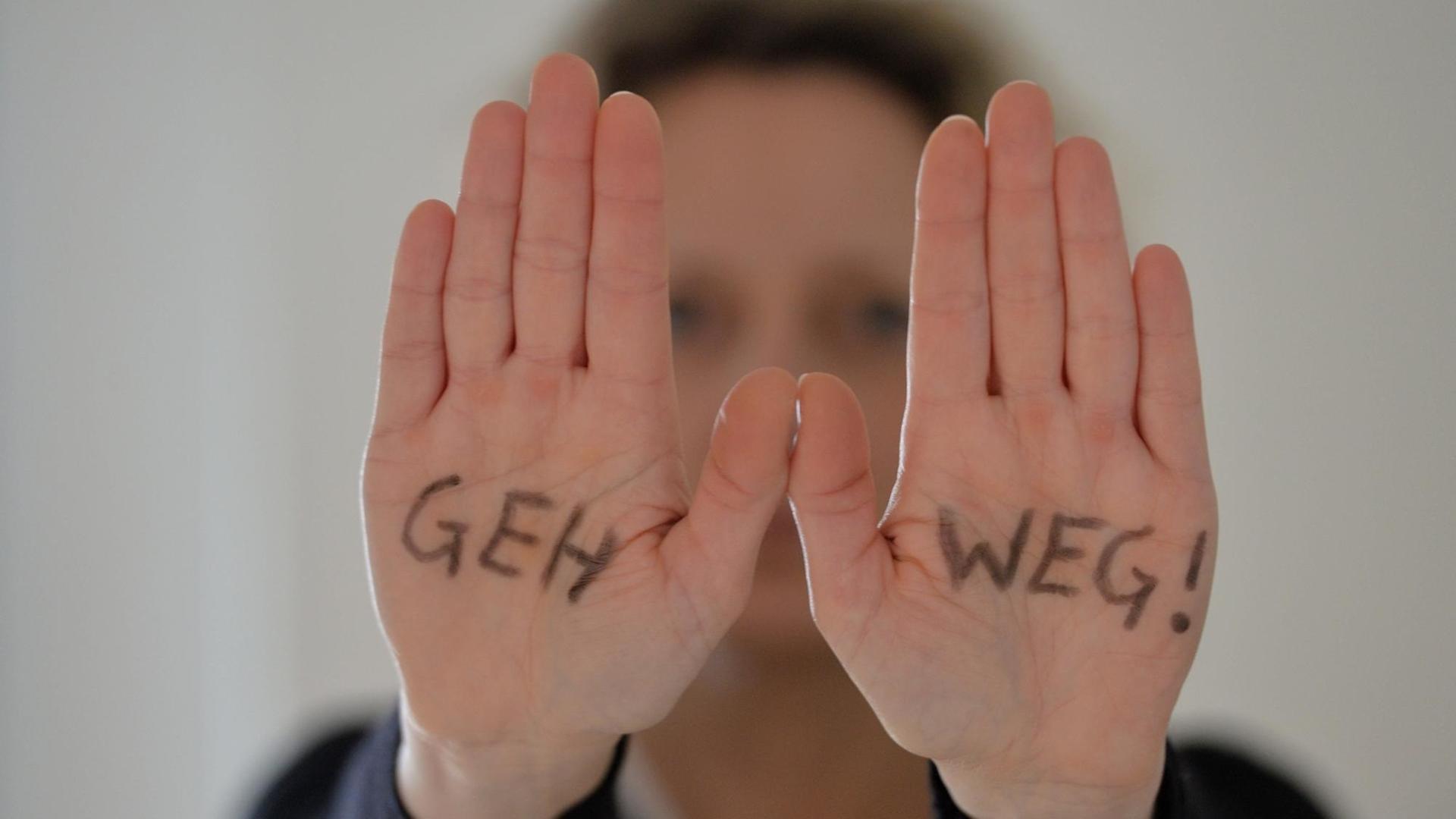Symbolfoto: Eine Frau steht mit ausgestreckten Armen da, auf ihren Händen steht geschrieben "Geh weg!" aufgenommen am 23.02.2016 in Osterode.