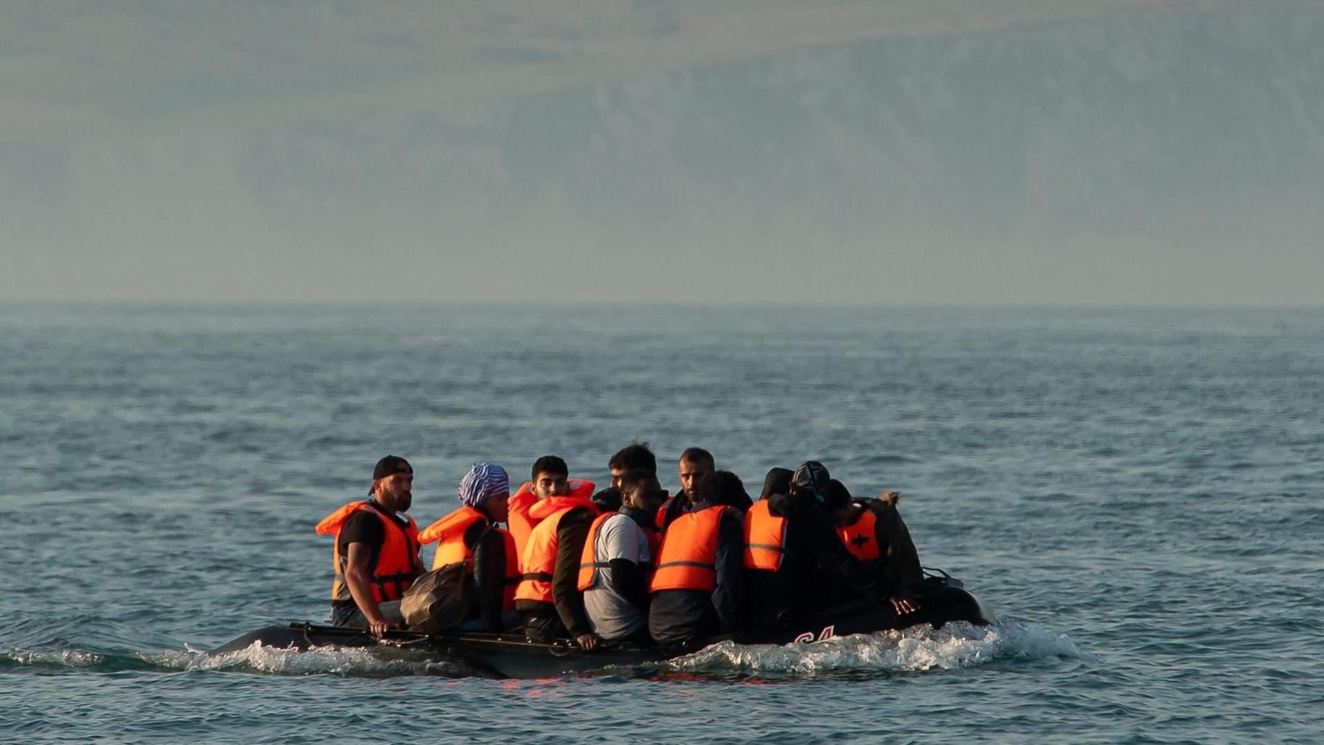 Die Flüchtlinge sitzen eng gedrängt in dem kleinen Schlauchboot, das aus der Ferne fotografiert ist. Sie tragen Schwimmwesten.