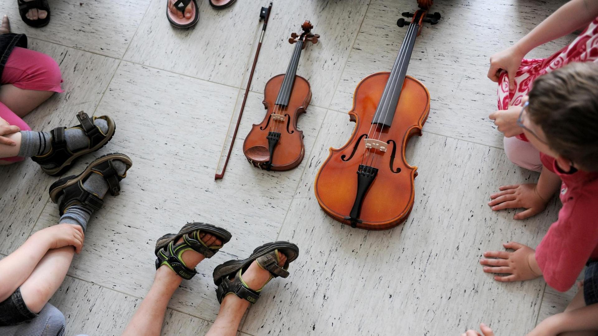 In der Musikschule. Kinder sitzen um zwei Streichinstrumente herum.