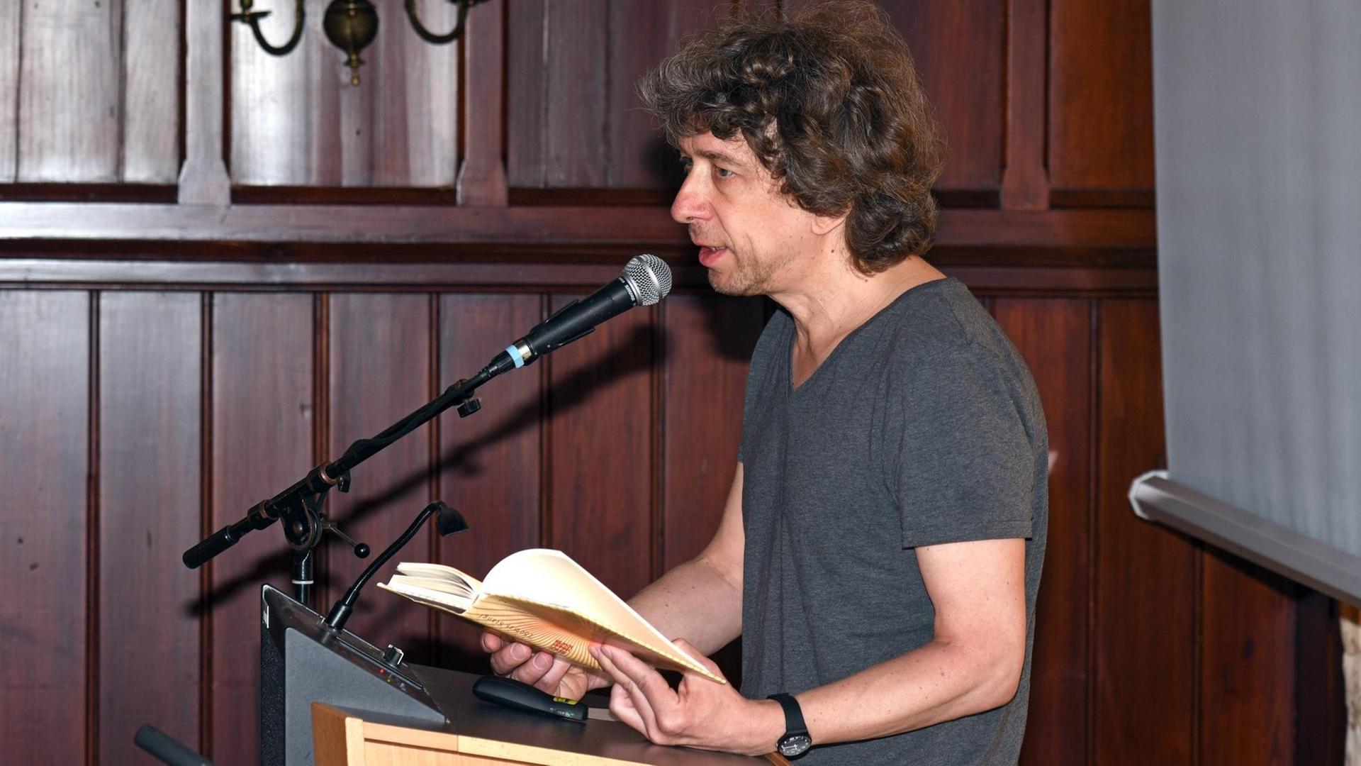 Der österreichische Autor Thomas Stangl steht hinter einem Pult und liest aus einem Buch vor.