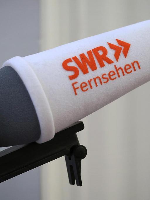 Man sieht ein Mikrofon mit einem weißen Windschutz, auf dem in roten Buchstaben "SWR Fernsehen" steht.