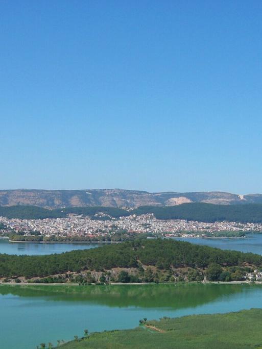 Eine idyllische, hügelige Landschaft mit Städtchen rund um einen See.