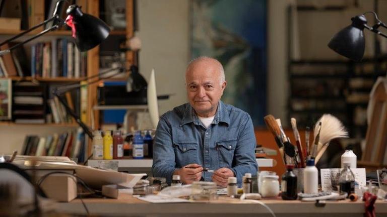 Der Künstler Yadegar Asisi sitzt an seinem Schreibtisch.