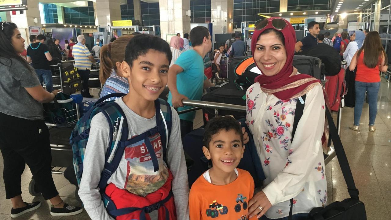 Omar, Ahmed und Judy Ghoniem stehen im Flughafen in Kairo und blicken in die Kamera