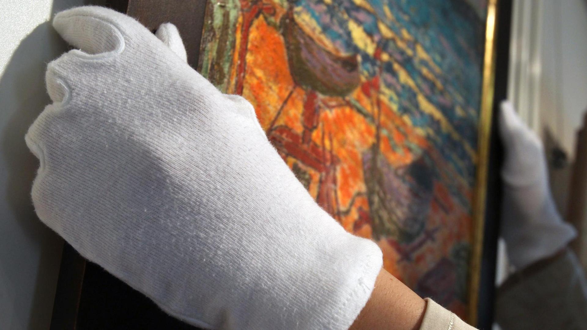 Mit weißen Stoffhandschuhen hängt eine Mitarbeiterin der Ahrenshooper Kunstauktionen ein zu versteigerndes Bild auf.