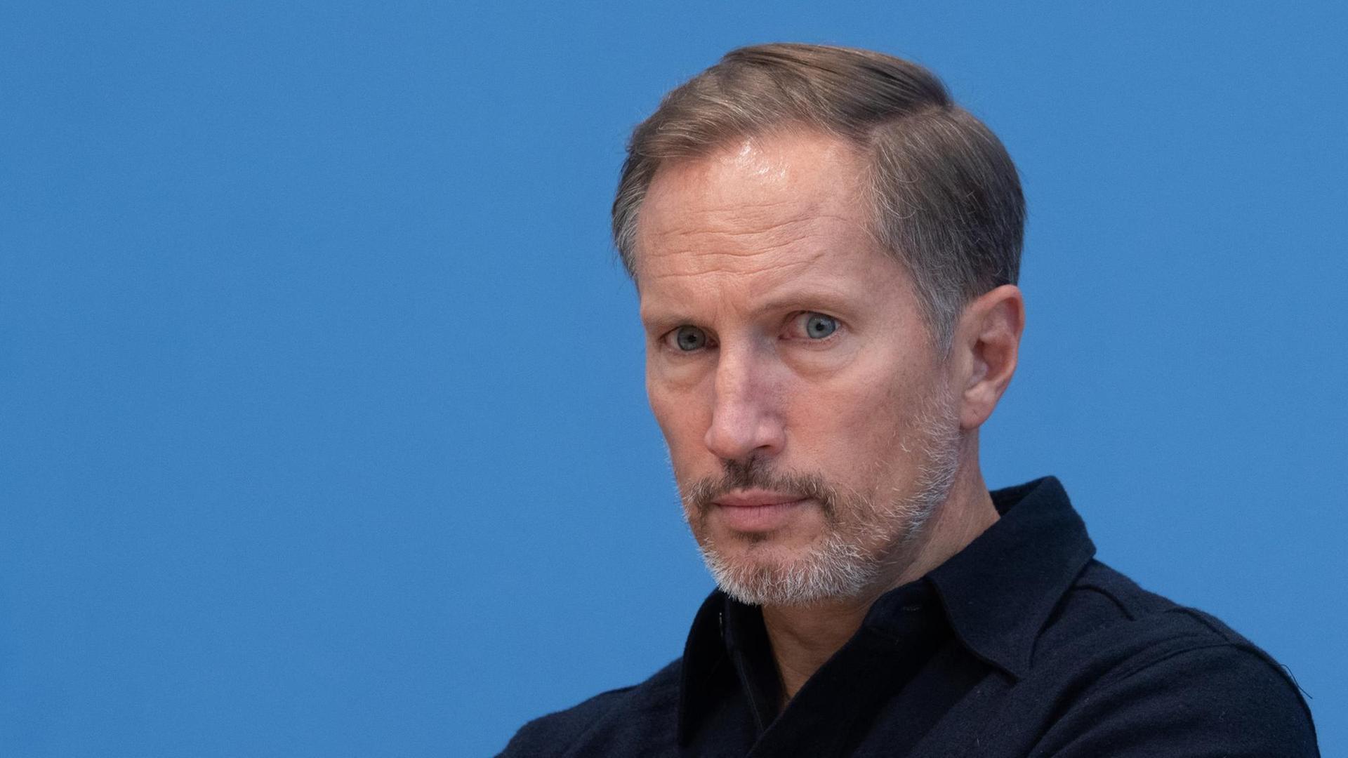 Porträtfoto des Schauspielers Benno Fürmann vor blauem Hintergrund während einer Pressekonferenz.