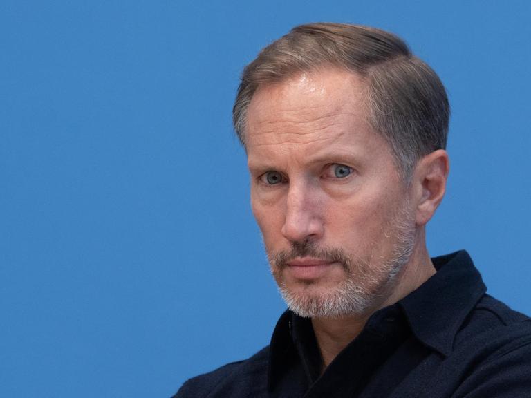Porträtfoto des Schauspielers Benno Fürmann vor blauem Hintergrund während einer Pressekonferenz.
