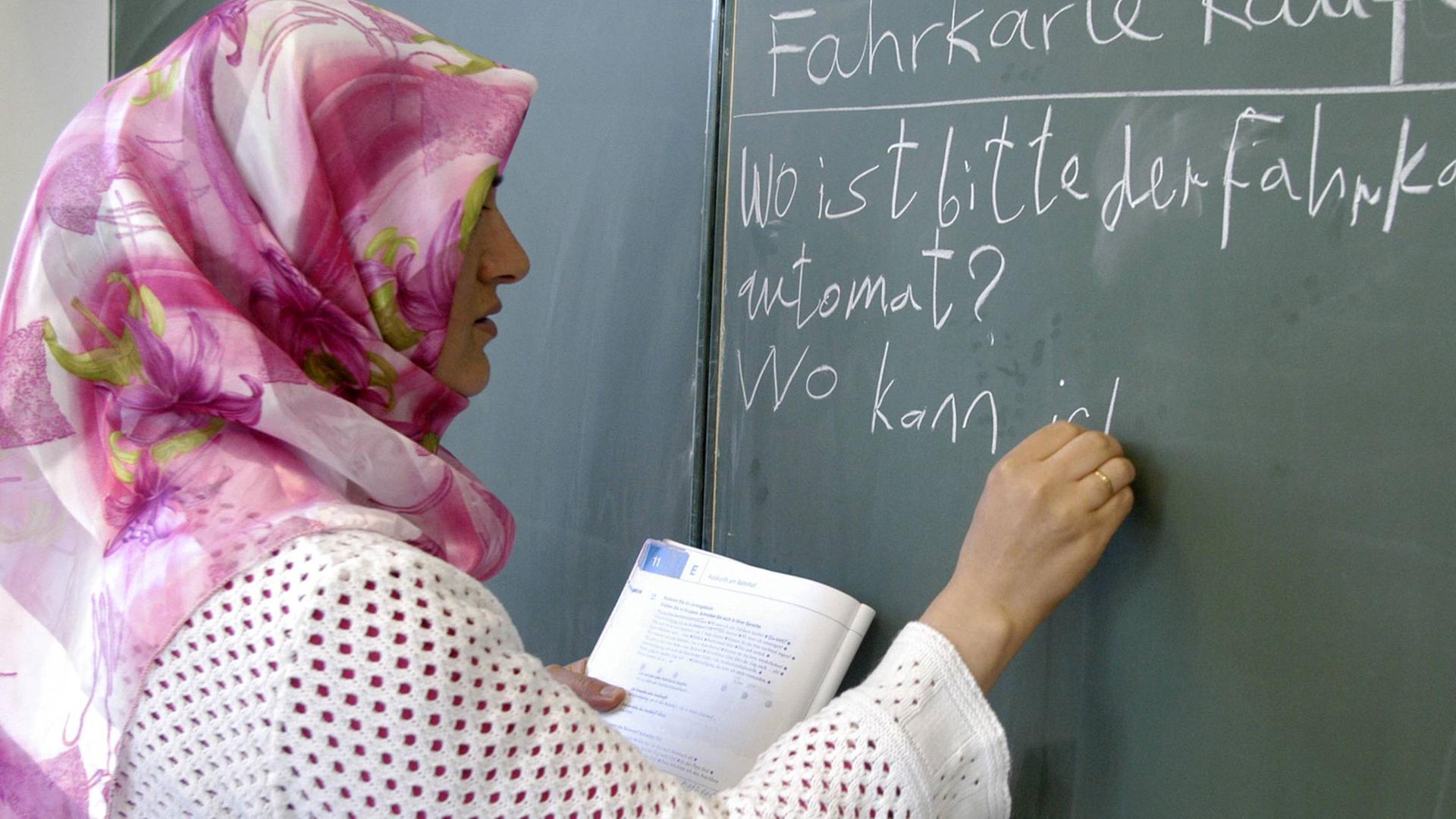 Eine Lehrerin mit Kopftuch schreibt an eine Tafel.