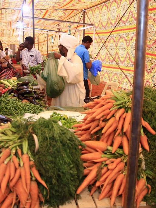 Ein Marktzelt in der sudanesischen Hauptstadt Khartoum . Ein Bauer verkauft an einem Tisch Möhren und anderes Gemüse.