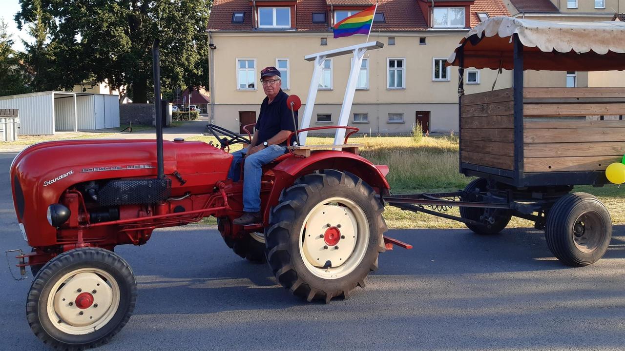 Ein Landwirt fährt auf seinem roten Traktor, der mit einer Regenbogenfahne geschmückt ist 