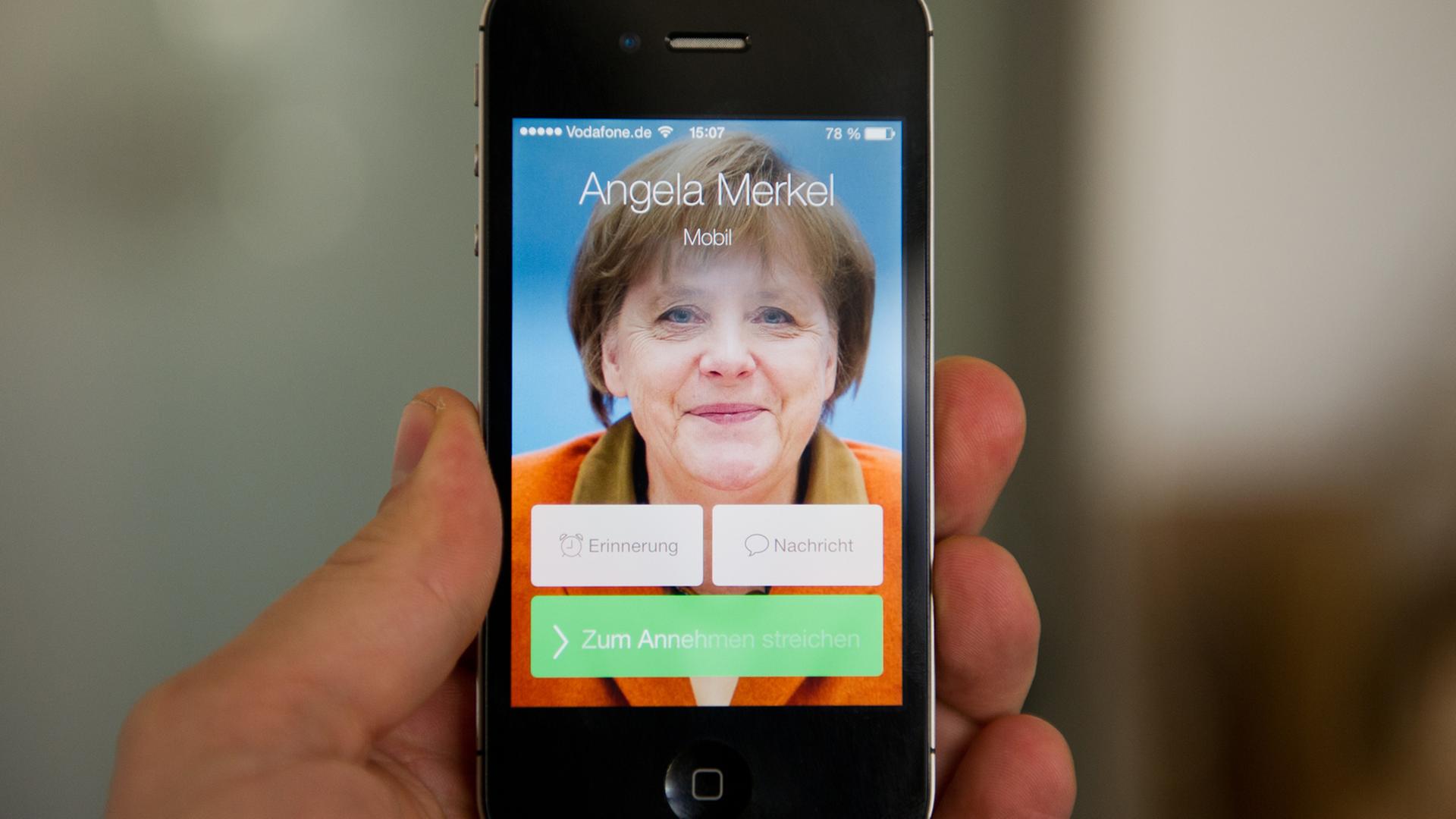Ein Mann hält ein Apple iPhone 4S, auf dem der fiktive Kontakt Angela Merkel anruft und ein Bild der Bundeskanzlerin zu sehen ist. Ein Mann hält ein Apple iPhone 4S, auf dem der fiktive Kontakt Angela Merkel anruft und ein Bild der Bundeskanzlerin zu sehen ist.