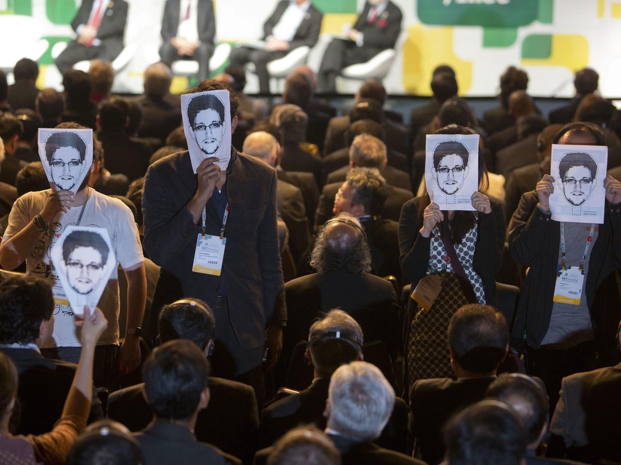 Teilnehmer der Internetkonferenz NETmundial in São Paulo, Brasilien, halten Poster mit dem Porträt des ehemaligen NSA-Mitarbeiters Edward Snowden vor ihr Gesicht.