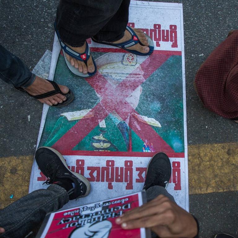 Diverse Füße von Demonstranten treten auf ein Plakat mit dem Konterfei General Min Aung Hlaing in der Nähe des Rathauses von Rangoon im Februar 2021.