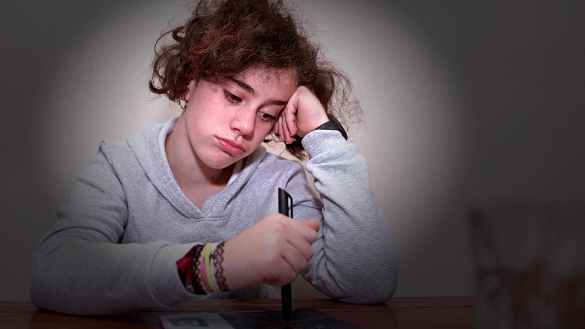 Unterricht von Zuhause in Corona-Zeiten: Ein Schulkind sitzt am Tisch, guckt traurig-gelangweilt und stützt den Kopf in die Hand (Symbolbild)