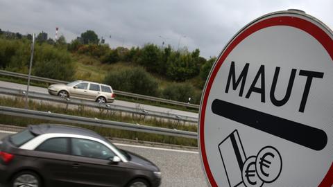 Ein Schild mit der Aufschrift "Maut" steht an einer Autobahn, im Hintergrund fahren Autos vorbei.