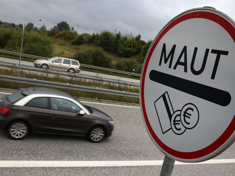 Ein Schild mit der Aufschrift "Maut" steht an einer Autobahn, im Hintergrund fahren Autos vorbei.