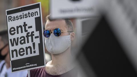 Ein Mann verfolgt eine Ansprache bei der offiziellen Gedenkveranstaltung zu den rassistisch motivierten Anschlägen in Hanau. Dabei hält er ein Schild mit der Aufschrift «Rassisten entwaffnen» in der Hand. Unter dem Motto «Erinnerung - Gerechtigkeit - Aufklärung - Konsequenzen» versammelten sich die Teilnehmer auf einem Platz in der Innenstadt. Aufgrund der aktuellen Corona-Infektionszahlen war die Teilnehmerzahl von der Behörden begrenzt worden.