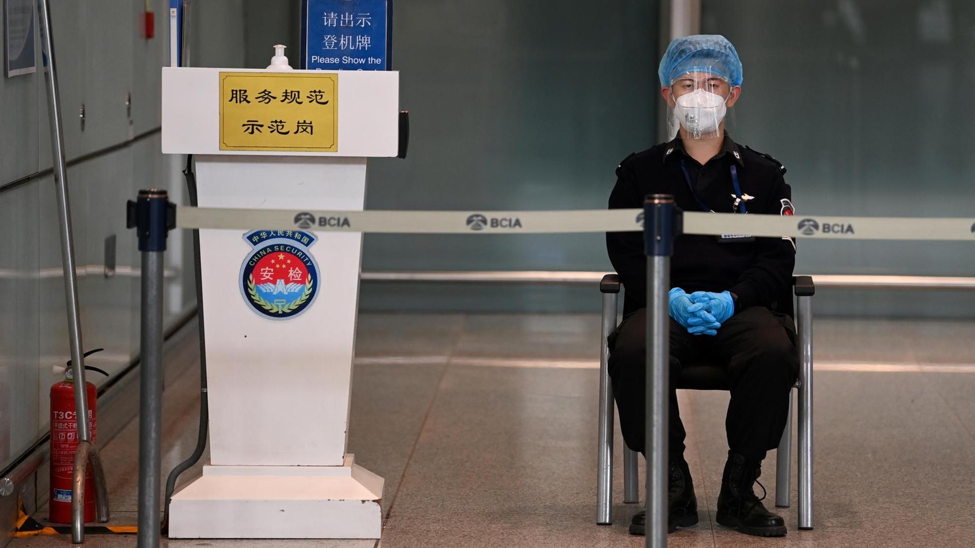Flughafen Peking: Ein Sicherheitsbeamter sitzt in Schutzkleidung an einer Kontrollstelle.