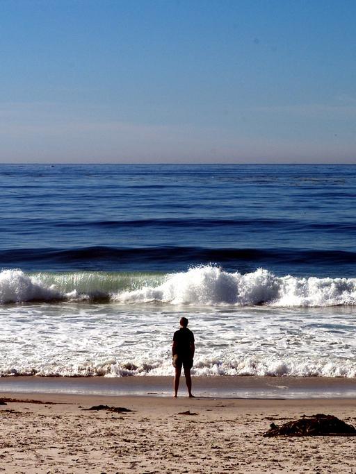 Eine Mann steht am Pazifikstrand von Carmel in Kalifornien und blickt aufs Meer