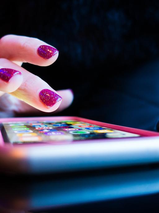 Ein Frauenhand mit violett lackierten Fingernägeln tippt auf ein Smartphone.