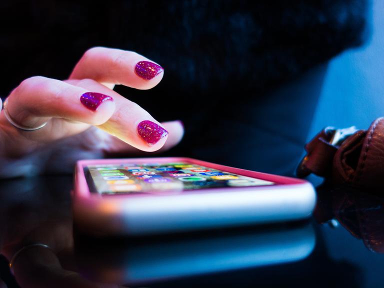 Ein Frauenhand mit violett lackierten Fingernägeln tippt auf ein Smartphone.
