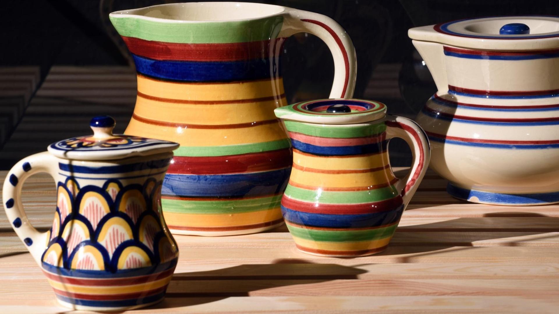 Farbenfrohe Keramik-Kannen auf einem Holztisch.
