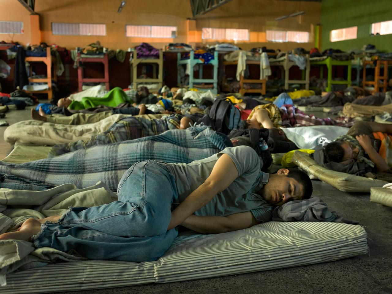 Dutzende Menschen schlafen auf Matratzen und Doppelstockbetten in einem großen Schlafsaal in einem christlichen Heim für Migranten in Tijuana, Mexiko.