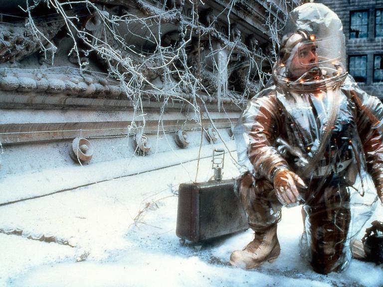 Szene aus dem Film "12 Monkeys". Der Schauspieler Bruce Willis in Schutzausrüstung befindet sich in einer verschneiten und menschenleeren Großstadt.