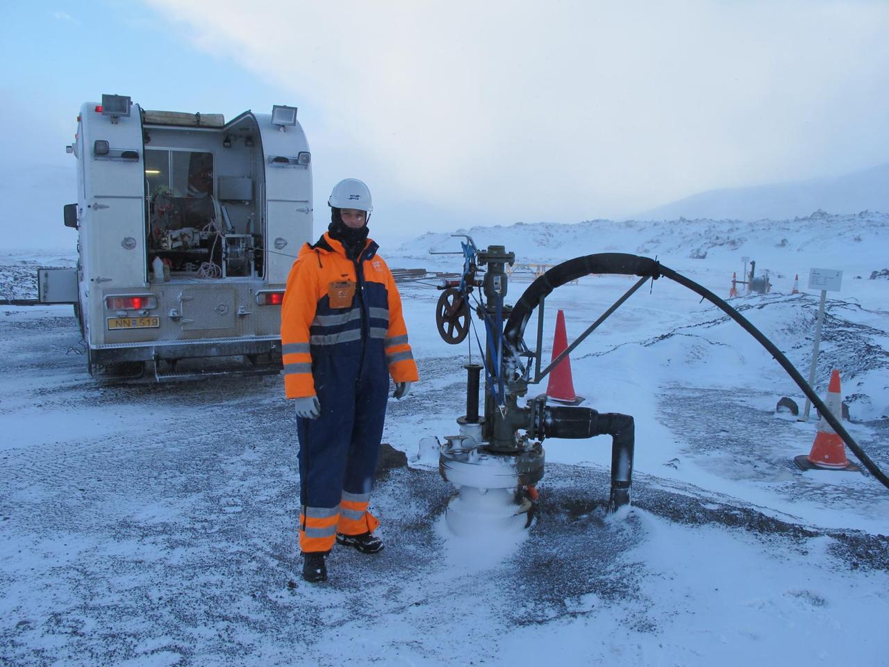 Ein Forscher in dicker Kleidung im verschneiten Island und neben ihm der Schlauch mit dem 2011 CO2 in den Boden gepumpt wurde.