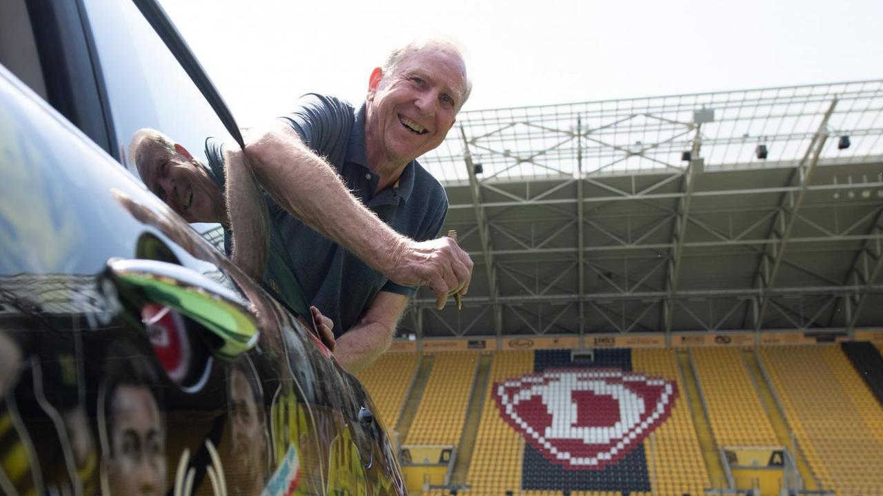 Dynamo-Legende Klaus Sammer lehnt sich im Stadion lachend aus einem Mini-Cooper. 