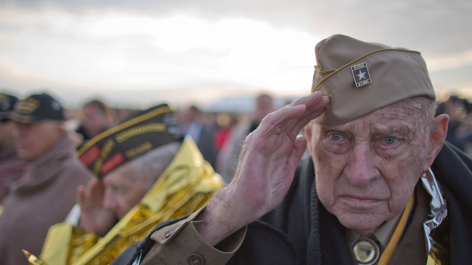 Weltkriegsveteran Raymond Sylvester aus den USA salutiert am 05.06.2014 während einer Gedenkveranstaltung am Utah Beach in der Normandie in Frankreich, eingehüllt in eine Wärmedecke.