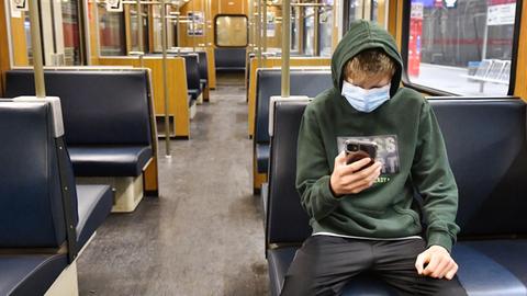 Ein Jugendlicher ist in einer leeren U-Bahn in München unterwegs und blickt auf sein Smartphone.