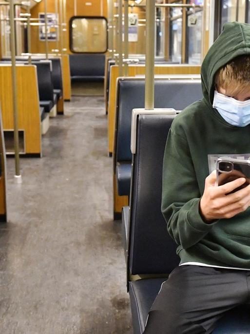 Ein Jugendlicher ist in einer leeren U-Bahn in München unterwegs und blickt auf sein Smartphone.