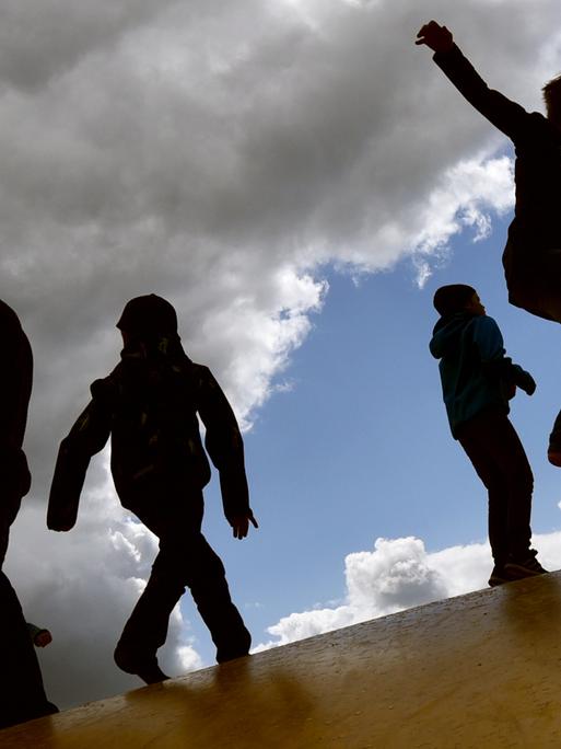 Kinder springen am 17.05.2015 bei wechselhaftem Wetter auf einer Hüpfburg in Elstal (Brandenburg) und heben sich dabei als Schatten vom Himmel ab.