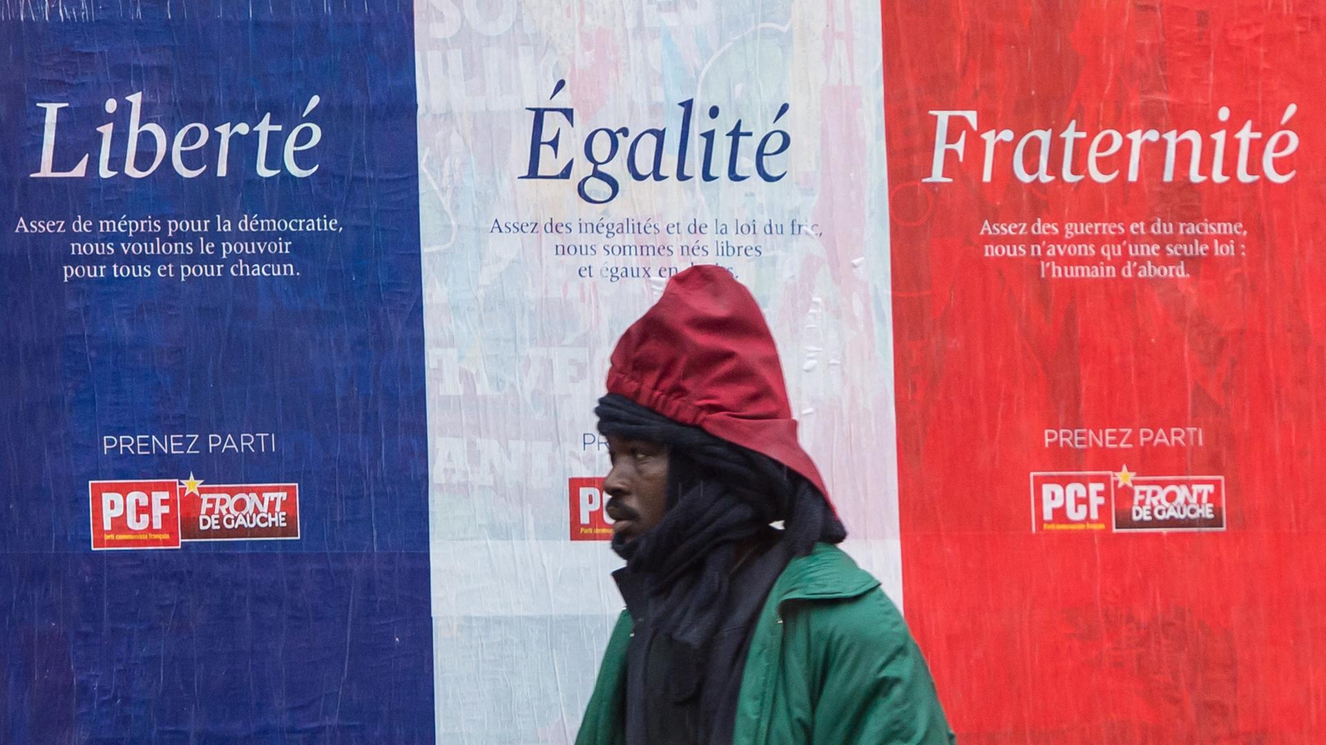 Ein Migrant geht vor einem Plakat mit den Worten "Liberé, Égalité, Fraternité" in Calais.