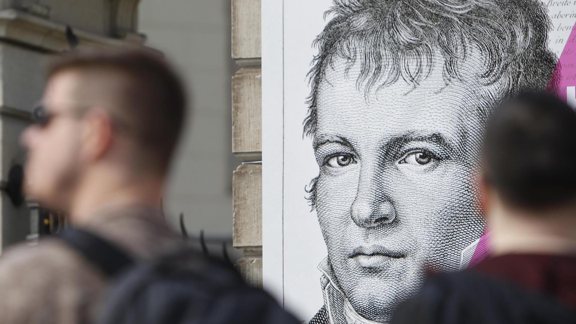 Menschen gehen an einer Plakatwand mit einem Bild des preußischen Forschers, Geographen und Naturforschers Alexander von Humboldt vorbei.