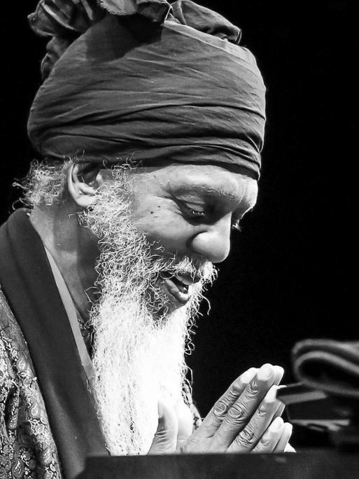 Mit Turban und weißem Bart, die Hände gefaltet, die Augen geschlossen sitzt Dr. Lonnie Smith vor seiner Orgel.