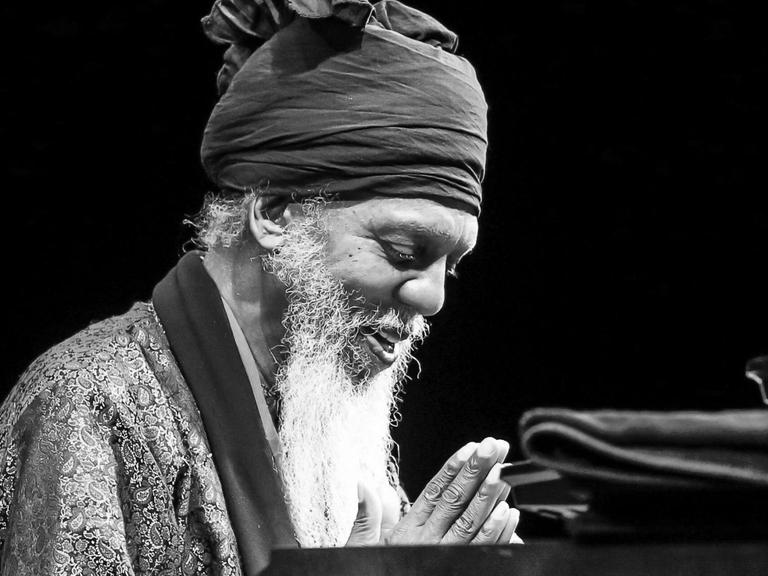 Mit Turban und weißem Bart, die Hände gefaltet, die Augen geschlossen sitzt Dr. Lonnie Smith vor seiner Orgel.