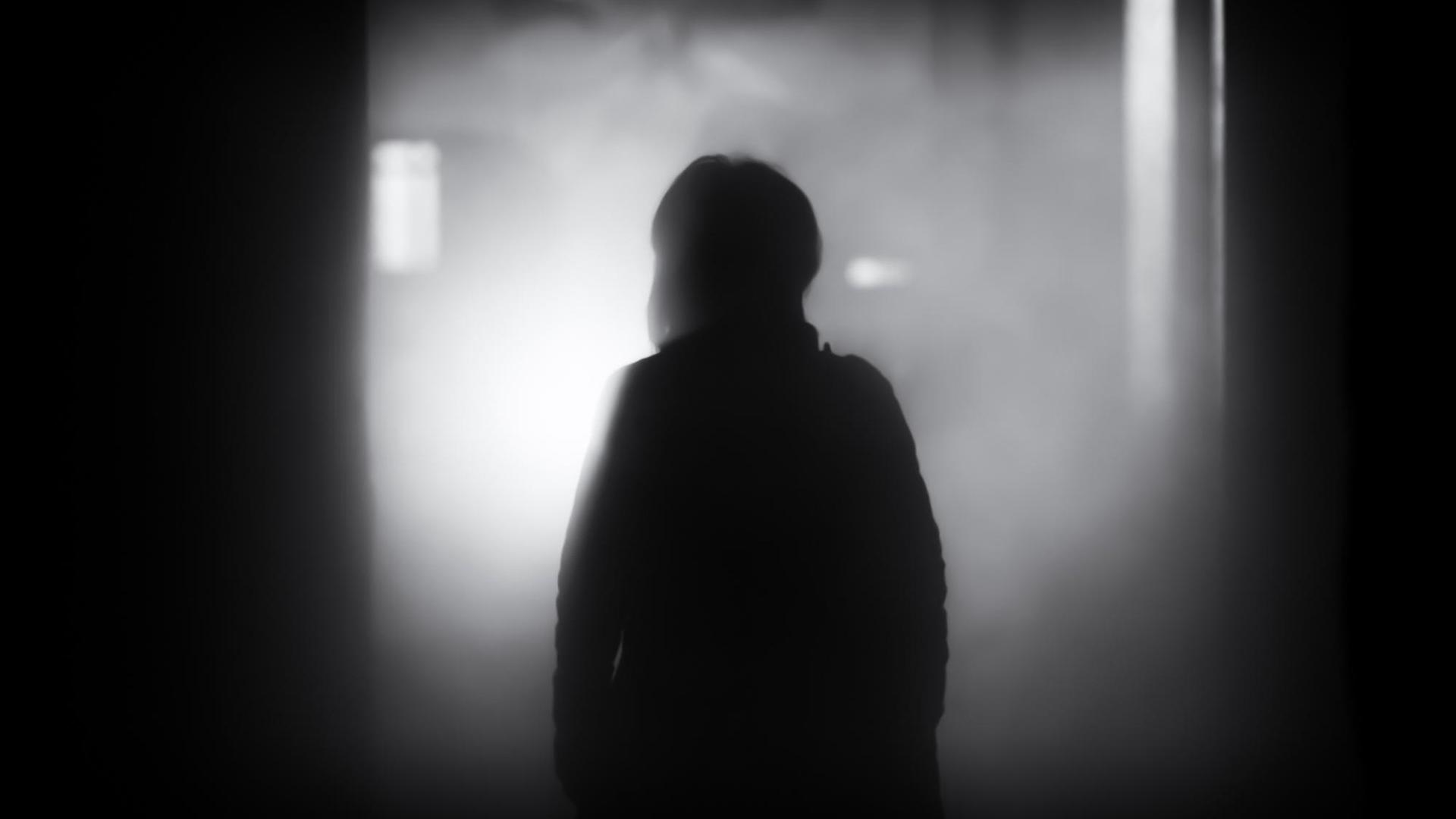 Ein Mensch geht aus dem Dunkeln auf eine Lichtquelle zu, die im Nebel liegt.