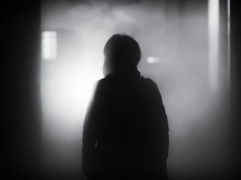 Ein Mensch geht aus dem Dunkeln auf eine Lichtquelle zu, die im Nebel liegt.