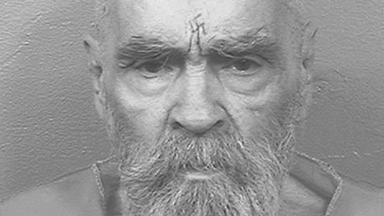 Charles Manson steht vor einer weißen Wand, auf der Stirn trägt er ein Hakenkreuz-Tattoo