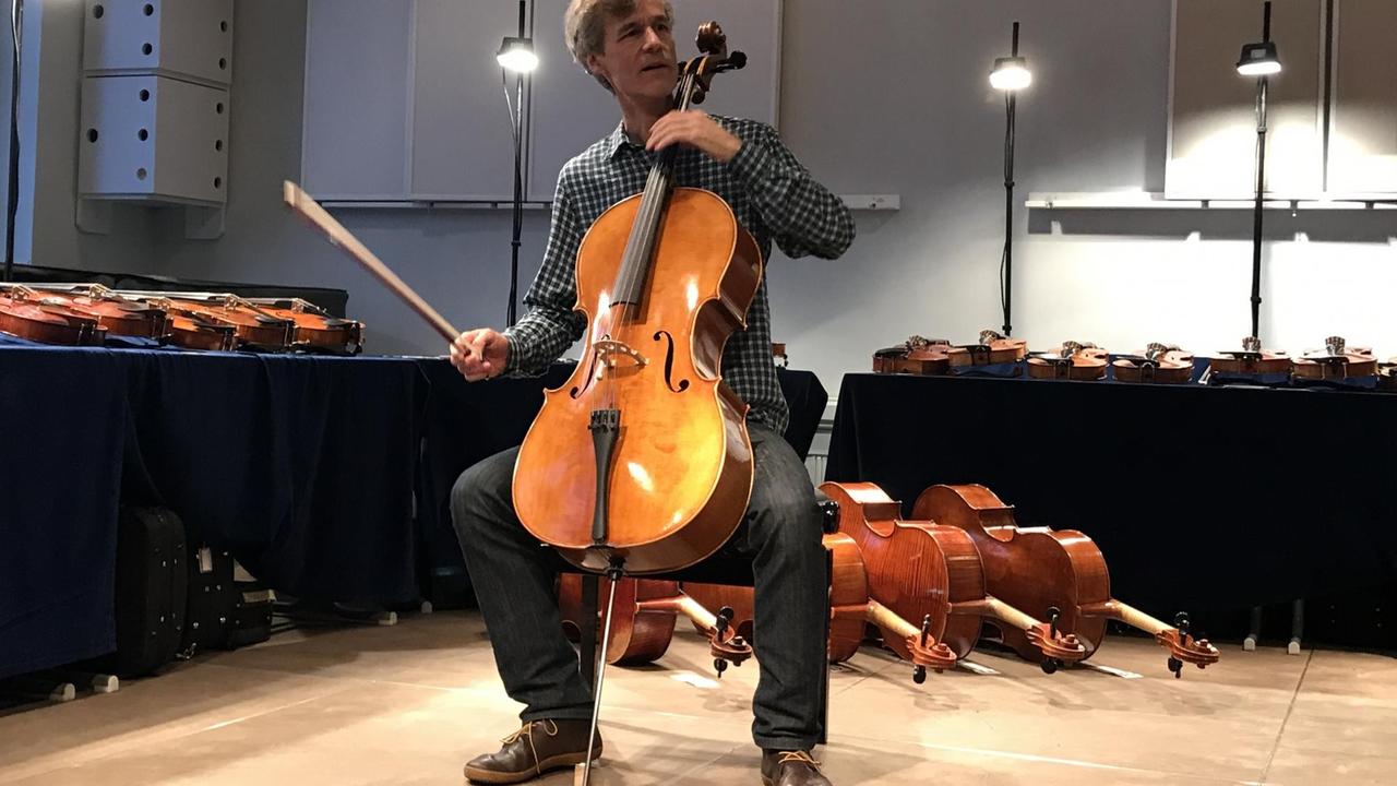 Ein Cellist probiert ein Instrument, mehrere Celli liegen für weitere Proben hinter ihm bereit.