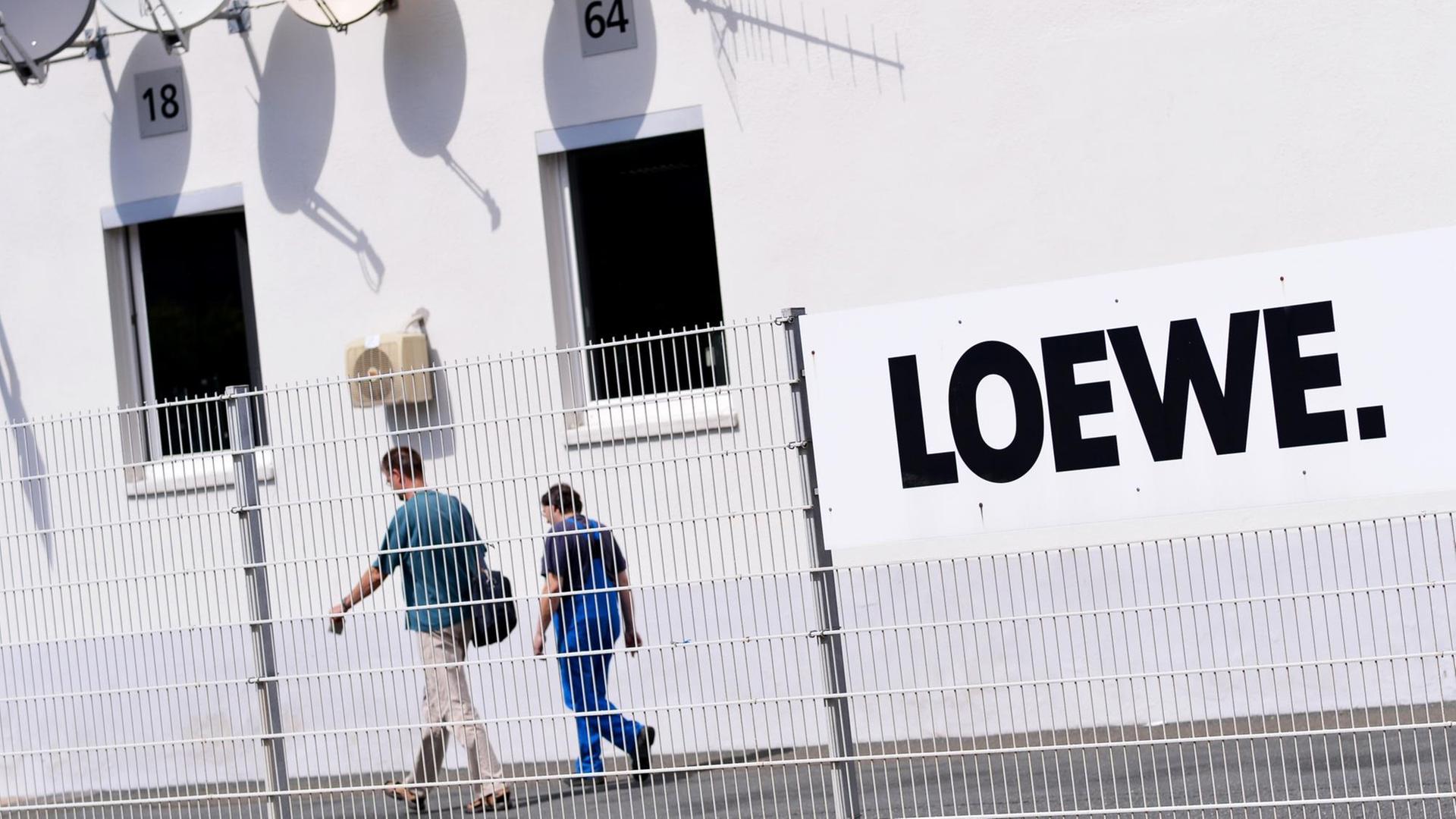 Zwei Mitarbeiter gehen über das Gelände des Elektronikherstellers Loewe AG, dessen Schriftzug groß an der Wand gesehen.