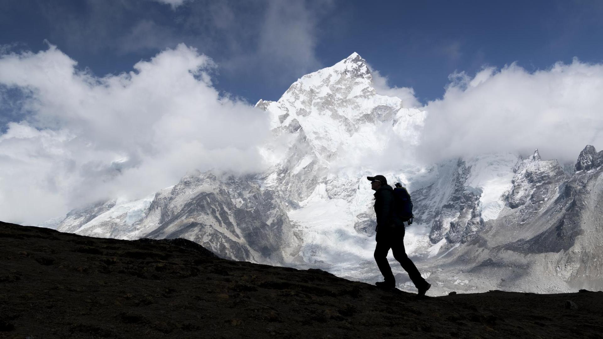 Im Vordergrund die Silhouette eines Bergsteigers, im Hintergrund der schneebedeckte Gipfel des Mount Everest