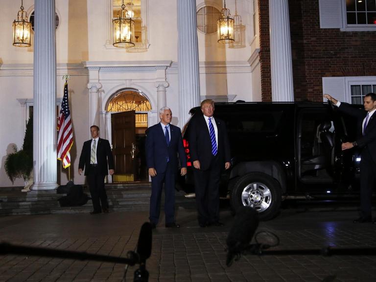 Sie sehen den designierten US-Präsidenten Trump und seinen angehenden Vize, sie kommen aus einem Haus, es ist dunkel draußen.