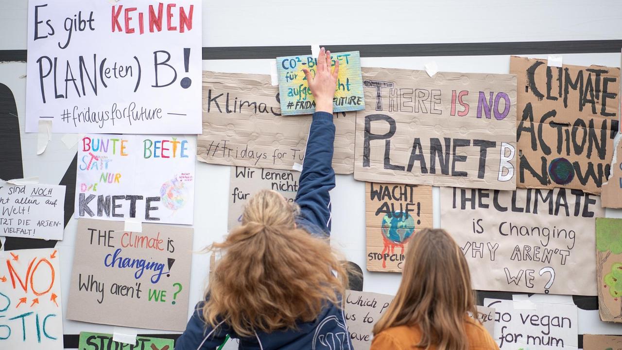 18.01.2019, Baden-Württemberg, Stuttgart: Zwei Schülerinnen kleben während einer Demonstration von Schülern gegen den Klimawandel Plakate an eine Wand. Die Aktion steht unter dem Motto "Fridays for future".
