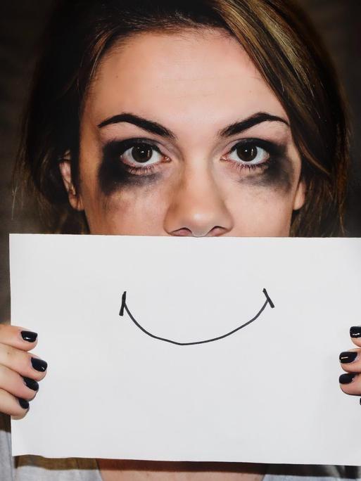 Eine Frau hält sich mit verschwischtem Makeup ein Smileymund vor das Gesicht.